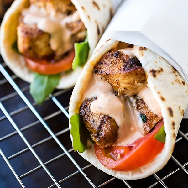 Two Wok & Sizzle Indian chicken wraps with sauce, tomato, and lettuce on a grill.