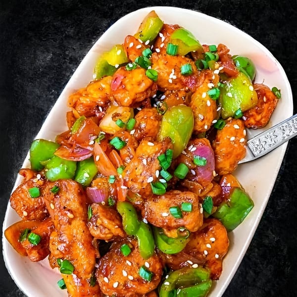 Wok & Sizzle's chili paneer, with bell peppers, onions, and sesame seeds, served on a white platter.