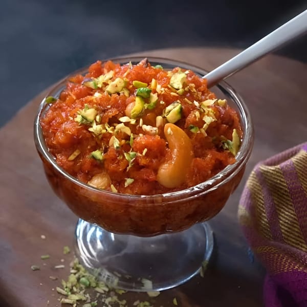 A glass bowl of vibrant orange Gajar Halwa, an Indian dessert, topped with pistachios and cashews.