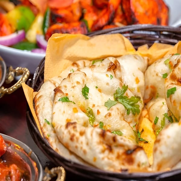 Basket of warm, garlic naan bread with cilantro, alongside other Indian dishes.