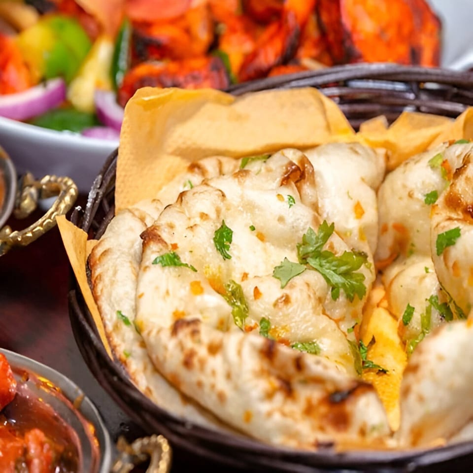 Basket of warm, garlic naan bread with cilantro, alongside other Indian dishes.